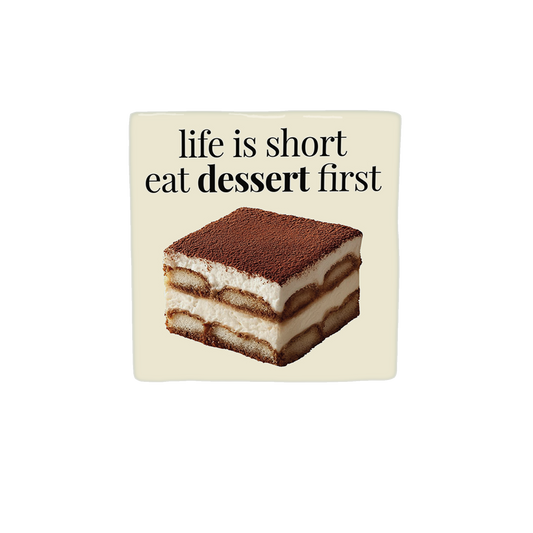 Decoratietegel – 10 x 10 cm - Op deze decoratietegel staat de tekst "life is short eat dessert first" in zwarte letters met een schreeflettertype. Daaronder is een realistische afbeelding van een vierkant stuk tiramisu geplaatst. Het ontwerp is gecentreerd op een crèmekleurige achtergrond.