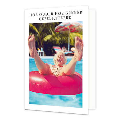 Op deze wenskaart staat een vrouw die in een roze opblaasband ligt met haar benen in de lucht. Om de afbeelding heen staat een wit kader. Bovenin het witte kader staat in het zwart de tekst 'Hoe ouder hoe gekker gefeliciteerd'.