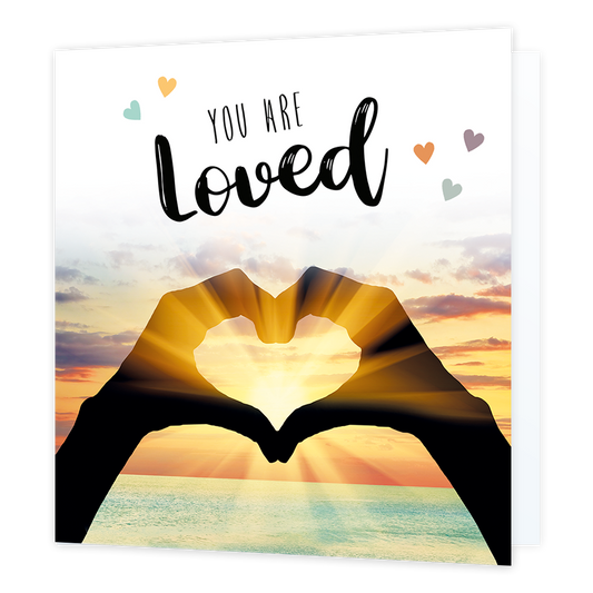 You are loved - Formaat: Normaal - Vorm: Vierkant - Liefdeskaart - Op deze wenskaart staat de zee met op de voorgrond twee handen die een hartje vormen waar de zon doorheen schijnt. In de illustratie staat de tekst: "You are loved". - Snelwenskaart