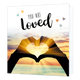 You are loved - Formaat: Standaard - Vorm: Vierkant - Liefdeskaart - Op deze wenskaart staat de zee met op de voorgrond twee handen die een hartje vormen waar de zon doorheen schijnt. In de illustratie staat de tekst: "You are loved". - Snelwenskaart