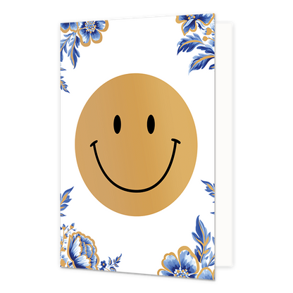Smiley - Formaat: Normaal - Vorm: Staand - Blanco kaart - Op deze wenskaart staat centraal een grote, goudkleurige smiley afgebeeld met een zwarte glimlach en zwarte ogen. De hoeken van de kaart zijn gedecoreerd met blauw-witte bloemen en bladeren in de stijl van Delfts blauw, die zijn afgewerkt met fijne gouden randen. De achtergrond van de gehele illustratie is effen wit. - Snelwenskaart