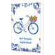 Met pensioen gefeliciteerd - Formaat: Normaal - Vorm: Staand - Pensioenkaart - Op deze wenskaart staat centraal een damesfiets afgebeeld die volledig is gedecoreerd met blauw-witte bloemmotieven in Delfts blauwe stijl en goudkleurige details. Aan het stuur hangt een goudkleurige mand gevuld met felrode tulpen en groene bladeren. De randen en hoeken van de kaart zijn rijkelijk versierd met bijpassende blauwe bloemen en bladeren met gouden accenten tegen een witte achtergrond. Onderaan de illustratie staat i