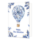 Happy New Adventure - Formaat: Normaal - Vorm: Staand - Succes kaart - Op deze wenskaart staat centraal een heteluchtballon afgebeeld waarvan de ballon volledig is gedecoreerd met een blauw-wit bloemenpatroon in de stijl van Delfts blauw met goudkleurige accenten. Aan de ballon hangt een traditionele, bruin gevlochten mand met dunne touwen. De vier hoeken van de kaart zijn versierd met bijpassende blauwe bloemen en bladeren met gouden randen tegen een witte achtergrond. Onderaan de illustratie staat in bla