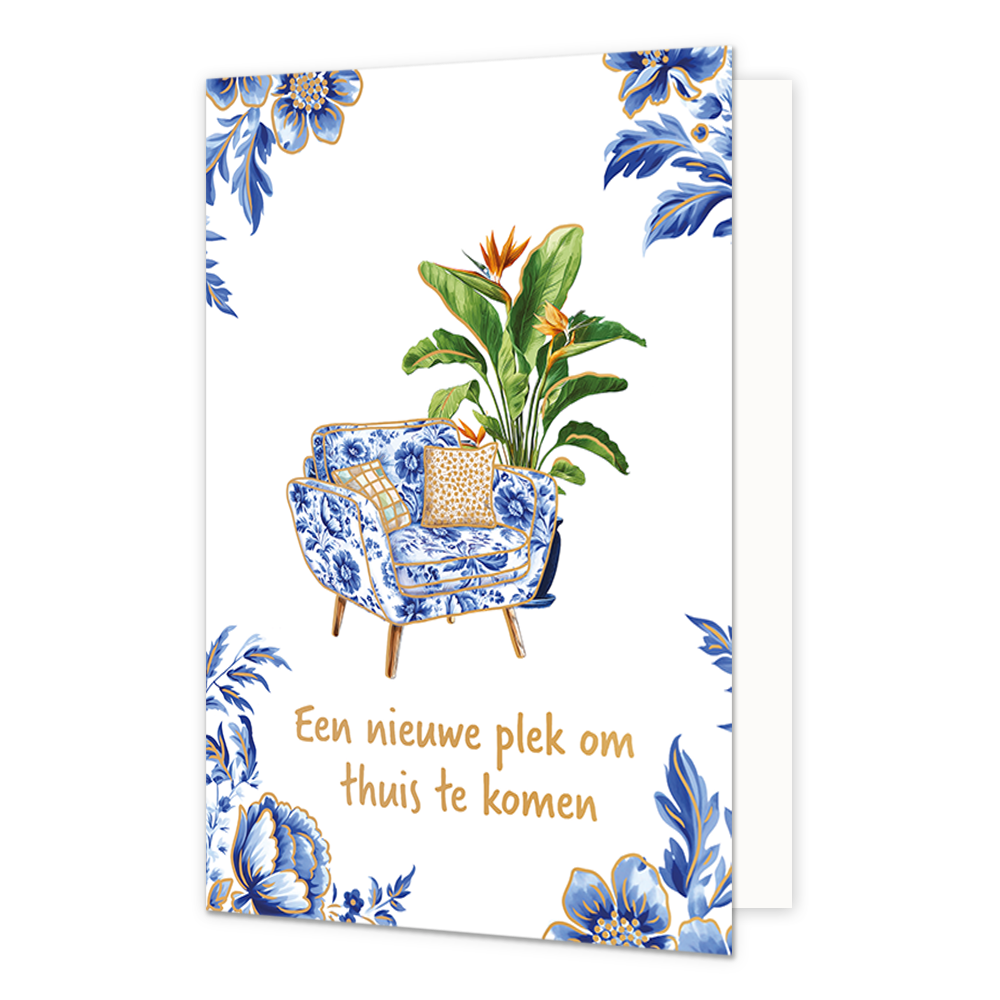 Een nieuwe plek om thuis te komen - Formaat: Normaal - Vorm: Staand - Woningkaart - Op deze wenskaart staat centraal een fauteuil afgebeeld die is bekleed met een blauw-wit bloemenpatroon in Delfts blauwe stijl, voorzien van twee kussens met een goudkleurig dessin en houten pootjes. Direct achter de stoel staat een grote, groene Strelitzia-plant (paradijsvogelbloem) met oranje-blauwe bloemen en goudkleurige randen langs de bladeren. De hoeken van de kaart zijn gedecoreerd met bijpassende blauwe bloemen en 