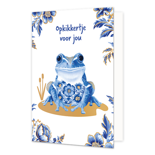 Opkikkertje voor jou - Formaat: Normaal - Vorm: Staand - Opkikker kaart - Op deze wenskaart staat centraal een kikker afgebeeld die is gedecoreerd met blauw-witte bloemmotieven in Delfts blauwe stijl en goudkleurige stippen op de poten en rug. De kikker zit op een goudkleurig vlak met daarnaast twee goudkleurige rietstengels, terwijl de hoeken van de kaart zijn versierd met bijpassende blauwe bloemen en bladeren met gouden randen tegen een witte achtergrond. Bovenaan de illustratie staat in blauwe, handges