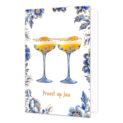 Proost op jou - Formaat: Normaal - Vorm: Staand - Proost kaart - Op deze wenskaart staan centraal twee cocktailglazen gevuld met een gele drank en een witte schuimlaag, die elk zijn gegarneerd met een halve passievrucht. De glazen zelf en de randen van de kaart zijn versierd met blauw-witte bloemmotieven in Delfts blauwe stijl en voorzien van fijne goudkleurige accenten. De gehele illustratie is geplaatst tegen een effen witte achtergrond. Onderaan de glazen staat in goudkleurige, handgeschreven letters de