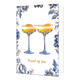 Proost op jou - Formaat: Normaal - Vorm: Staand - Proost kaart - Op deze wenskaart staan centraal twee cocktailglazen gevuld met een gele drank en een witte schuimlaag, die elk zijn gegarneerd met een halve passievrucht. De glazen zelf en de randen van de kaart zijn versierd met blauw-witte bloemmotieven in Delfts blauwe stijl en voorzien van fijne goudkleurige accenten. De gehele illustratie is geplaatst tegen een effen witte achtergrond. Onderaan de glazen staat in goudkleurige, handgeschreven letters de