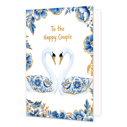 To the happy couple - Formaat: Normaal - Vorm: Staand - Huwelijkskaart - Op deze wenskaart staan centraal twee zwanen tegenover elkaar afgebeeld die met hun halzen een hartvorm vormen, waarbij hun vleugels gedecoreerd zijn met blauw-witte bloemmotieven in Delfts blauwe stijl en goudkleurige stippen. De snavels van de zwanen zijn goudkleurig met zwart, en de randen en hoeken van de kaart zijn rijkelijk versierd met bijpassende blauwe bloemen en bladeren met gouden accenten tegen een witte achtergrond. Boven