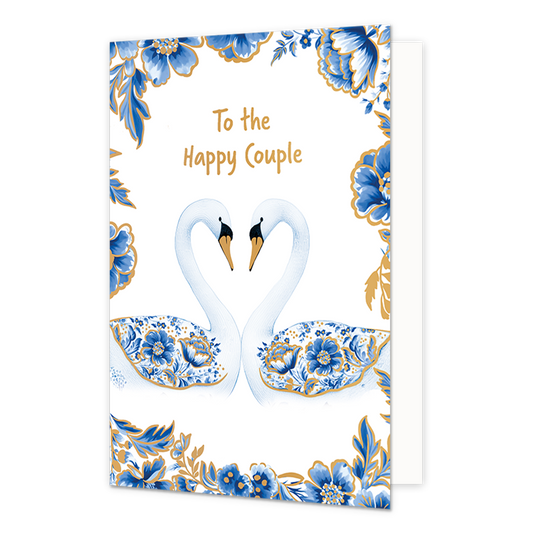 To the happy couple - Formaat: Normaal - Vorm: Staand - Huwelijkskaart - Op deze wenskaart staan centraal twee zwanen tegenover elkaar afgebeeld die met hun halzen een hartvorm vormen, waarbij hun vleugels gedecoreerd zijn met blauw-witte bloemmotieven in Delfts blauwe stijl en goudkleurige stippen. De snavels van de zwanen zijn goudkleurig met zwart, en de randen en hoeken van de kaart zijn rijkelijk versierd met bijpassende blauwe bloemen en bladeren met gouden accenten tegen een witte achtergrond. Boven