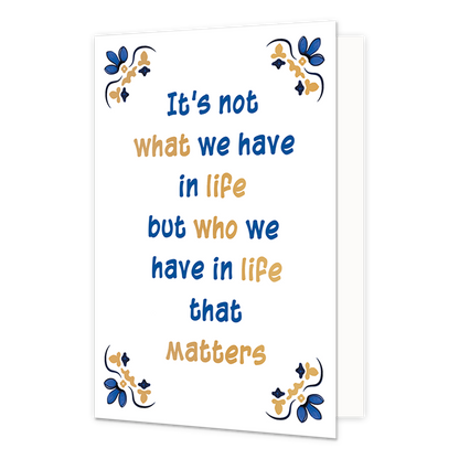 It's not what we have in life - Formaat: Normaal - Vorm: Staand - Denken aan kaart - Op deze wenskaart staat centraal een handgeschreven tekst in blauwe en goudkleurige letters tegen een effen witte achtergrond geschreven. De volledige tekst luidt onder elkaar: "It's not what we have in life but who we have in life that matters". In alle vier de hoeken van de kaart bevindt zich een symmetrisch, traditioneel ornament geïnspireerd op een tegelvlak, uitgevoerd in blauwe en goudkleurige tinten. - Snelwenskaart