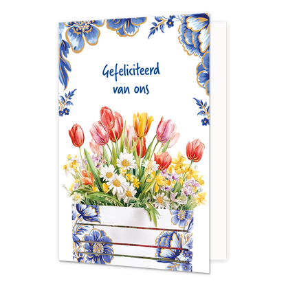 Gefeliciteerd van ons - Formaat: Normaal - Vorm: Staand - Felicitatiekaart - Op deze wenskaart staat aan de onderzijde een houten plantenbak of krat afgebeeld die gedecoreerd is met blauw-witte bloemmotieven in Delfts blauwe stijl en fijne goudkleurige lijntjes. De bak is gevuld met een gevarieerd voorjaarsboeket van rode, roze en gele tulpen, witte madeliefjes en andere kleine gele en paarse bloemetjes met groene bladeren. De randen en hoeken aan de bovenzijde van de kaart zijn op een witte achtergrond ve
