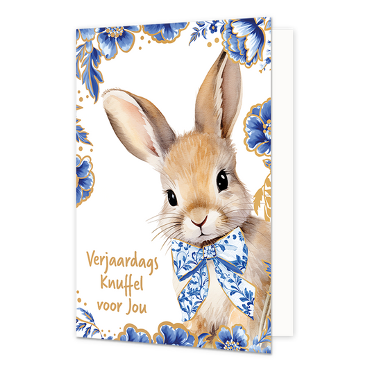 Verjaardags knuffel voor jou - Formaat: Normaal - Vorm: Staand - Verjaardagskaart - Op deze wenskaart staat aan de rechterzijde een getekend bruin konijn afgebeeld dat een grote strik om de hals draagt die gedecoreerd is met blauw-witte bloemmotieven in Delfts blauwe stijl. De randen en hoeken van de kaart zijn op een witte achtergrond rijkelijk versierd met bijpassende grote blauwe bloemen en bladeren met fijne goudkleurige randen. Aan de linkerzijde staat in goudkleurige letters onder elkaar de tekst "Ve