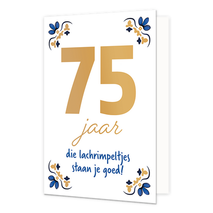 75 jaar - Formaat: Normaal - Vorm: Staand - Verjaardagskaart - Op deze wenskaart staat centraal het grote getal "75" in goudkleurige letters afgebeeld tegen een effen witte achtergrond. In de vier hoeken van de kaart bevindt zich een symmetrisch, traditioneel ornament in blauwe en goudkleurige tinten, geïnspireerd op een klassiek tegelontwerp. Onder het getal staat de handgeschreven tekst "jaar die lachrimpeltjes staan je goed!", waarbij het woord "jaar" in het goud is gedrukt en de zin "die lachrimpeltjes