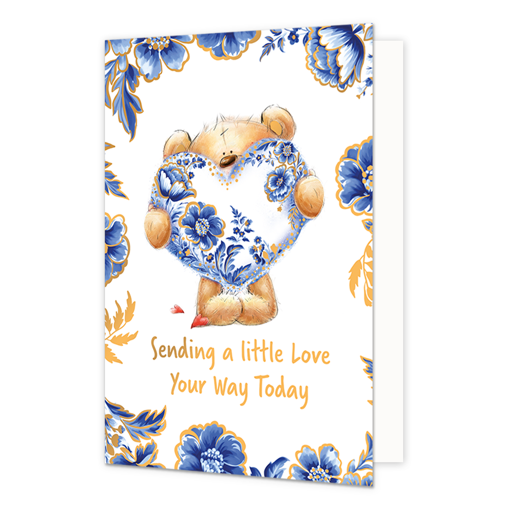 Sending a little love your way today - Formaat: Normaal - Vorm: Staand - Denken aan kaart - Op deze wenskaart staat centraal een schattige, zittende teddybeer afgebeeld, die een groot hart vasthoudt dat versierd is met gedetailleerde blauw-witte Delfts Blauwe bloemmotieven en gouden accenten. De beer zelf heeft een lichtbruine kleur en kijkt met grote, vriendelijke ogen naar voren, met kleine rode hartjes bij zijn poten. De randen en hoeken van de kaart zijn rijkelijk versierd met bijpassende grote blauwe 