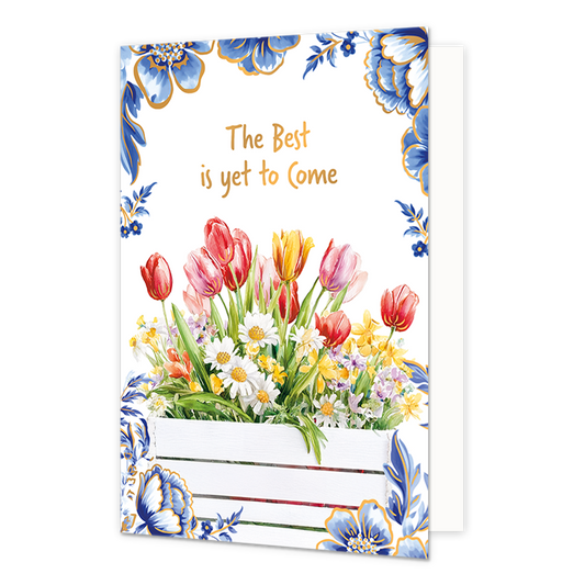 The best is yet to come - Formaat: Normaal - Vorm: Staand - Blanco kaart - Op deze wenskaart staat aan de onderzijde een witte houten plantenbak gevuld met een kleurrijk boeket van rode, roze en gele tulpen, witte madeliefjes en andere voorjaarsbloemen afgebeeld. De hoeken en randen van de kaart zijn op een witte achtergrond rijkelijk versierd met grote blauwe bloemen en bladeren in Delfts blauwe stijl met goudkleurige randen. Centraal aan de bovenzijde staat in goudkleurige letters onder elkaar de tekst "