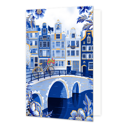 Op deze wenskaart is een sfeervol Nederlands stadsgezicht aan een gracht afgebeeld met karakteristieke grachtenpanden in blauwe en witte tinten met goudkleurige accenten. Op de stenen boogbrug over het water staat een fiets die is gedecoreerd met Delfts blauwe patronen en een mandje met rode tulpen aan het stuur. De hoeken en randen van de kaart zijn rijkelijk versierd met grote, gedetailleerde blauwe bloemen en bladeren met goudkleurige randen tegen een witte achtergrond.