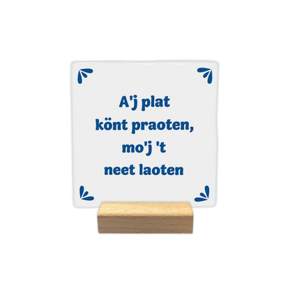 A'j plat könt praoten, mo'j 't neet loaten - Decoratie tegel - Formaat: - Op deze decoratie tegel staat de tekst "A'j plat könt praoten, mo'j 't neet laoten" in blauwe letters centraal afgebeeld. In elk van de vier hoeken is een klein, blauw decoratief element geplaatst dat bestaat uit drie bladvormige blaadjes. De achtergrond van de tegel is wit. - Snelwenskaart