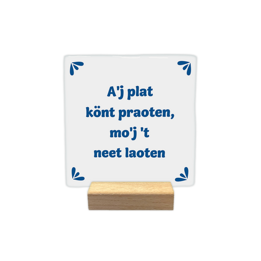 A'j plat könt praoten, mo'j 't neet loaten - Decoratie tegel - Formaat: - Op deze decoratie tegel staat de tekst "A'j plat könt praoten, mo'j 't neet laoten" in blauwe letters centraal afgebeeld. In elk van de vier hoeken is een klein, blauw decoratief element geplaatst dat bestaat uit drie bladvormige blaadjes. De achtergrond van de tegel is wit. - Snelwenskaart