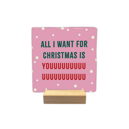 All I want for christmas is you - Decoratie tegel - Formaat: - Op deze decoratie tegel staat een roze achtergrond met kleine witte stippen. In het midden staat de tekst all i want for christmas is youuuu... in groene en rode letters geschreven. - Snelwenskaart