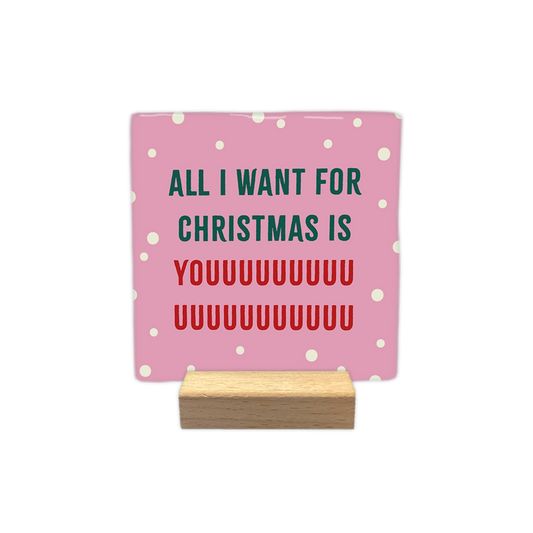 All I want for christmas is you - Decoratie tegel - Formaat: - Op deze decoratie tegel staat een roze achtergrond met kleine witte stippen. In het midden staat de tekst all i want for christmas is youuuu... in groene en rode letters geschreven. - Snelwenskaart