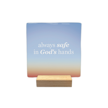 Always safe in God's hands - Decoratie tegel - Formaat: - Op deze decoratie tegel staat de tekst "always safe in God's hands" in witte letters. De woorden "safe" en "God's" zijn daarbij cursief weergegeven. De achtergrond heeft een kleurverloop van blauw aan de bovenzijde naar een warmere tint aan de onderzijde. - Snelwenskaart