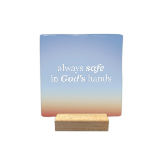 Always safe in God's hands - Decoratie tegel - Formaat: - Op deze decoratie tegel staat de tekst "always safe in God's hands" in witte letters. De woorden "safe" en "God's" zijn daarbij cursief weergegeven. De achtergrond heeft een kleurverloop van blauw aan de bovenzijde naar een warmere tint aan de onderzijde. - Snelwenskaart