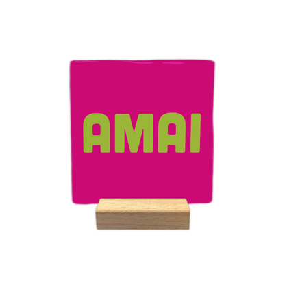 Amai - Decoratie tegel - Formaat: - Op deze decoratie tegel staat de tekst "AMAI" in grote, lichtgroene letters centraal afgebeeld. De achtergrond van de tegel is felroze van kleur. - Snelwenskaart