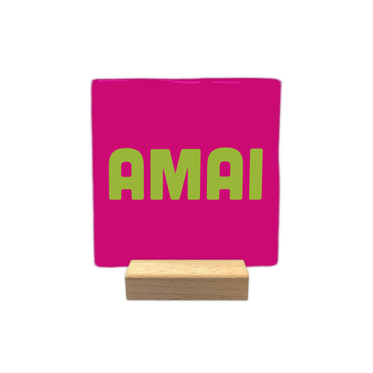 Amai - Decoratie tegel - Formaat: - Op deze decoratie tegel staat de tekst "AMAI" in grote, lichtgroene letters centraal afgebeeld. De achtergrond van de tegel is felroze van kleur. - Snelwenskaart