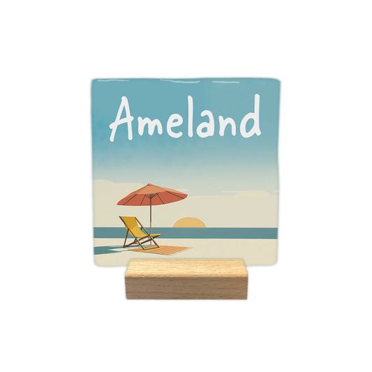 Ameland - Decoratie tegel - Formaat: - Op deze decoratie tegel staat de tekst "Ameland" in witte letters bovenaan afgebeeld. Onder de tekst is een strandscène te zien met een gele strandstoel, een oranje parasol en een gestreept kleedje op het zand. Op de achtergrond is een blauwe zee met een ondergaande zon zichtbaar. - Snelwenskaart