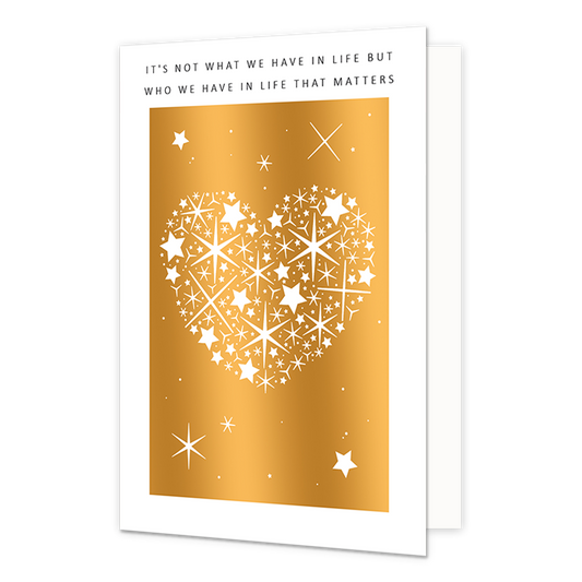 Op deze wenskaart staat een wit hart gevuld met sterren op goudfolie gedrukt. Het goudfolie wordt omringd door een witkader. Bovenaan op de kaart staat in het zwart de tekst 'It's not what we have in life but who we have in life that matters'.