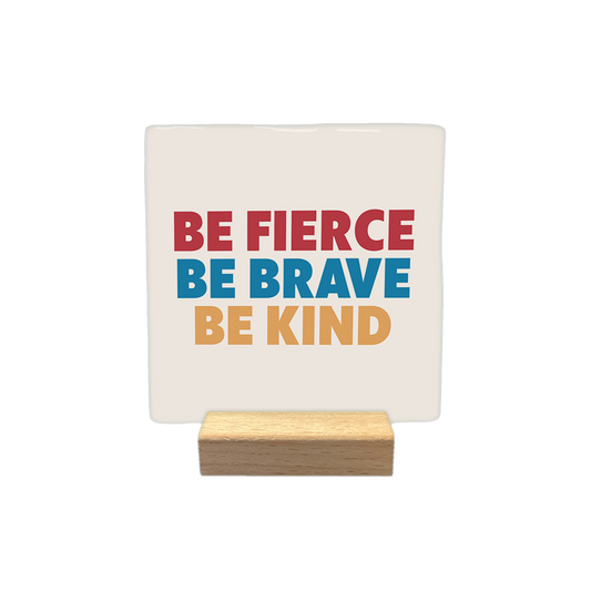 Be fierce be brave be kind - Decoratie tegel - Formaat: - Op deze decoratietegel staat de tekst "BE FIERCE", "BE BRAVE" en "BE KIND" onder elkaar in hoofdletters. De woorden zijn in drie verschillende kleuren uitgevoerd: de bovenste regel is rood, de middelste is blauw en de onderste is beige. De tekst is gecentreerd op een lichtbeige achtergrond. - Snelwenskaart
