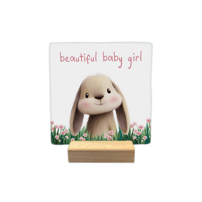 Beautiful baby girl - Decoratie tegel - Formaat: - Op deze decoratie tegel staat een illustratie van een schattig konijntje met lange oren en roze blosjes op de wangen, dat midden in een veld met groen gras en roze bloemen staat. Het konijntje kijkt vriendelijk naar voren tegen een witte achtergrond. Bovenaan de illustratie staat in een roze lettertype de tekst "beautiful baby girl" geschreven. - Snelwenskaart