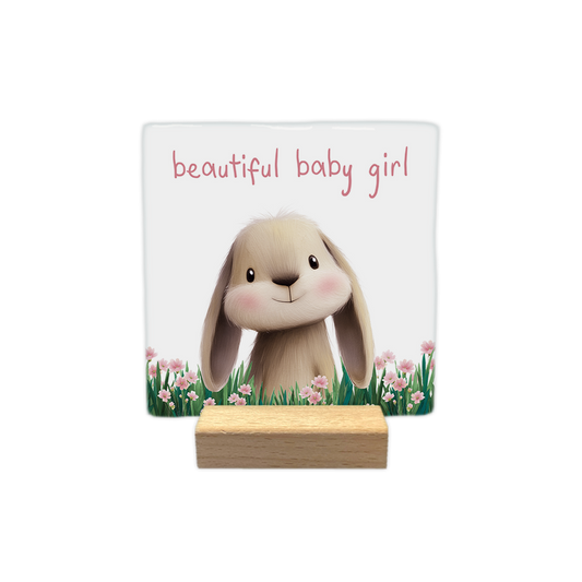 Beautiful baby girl - Decoratie tegel - Formaat: - Op deze decoratie tegel staat een illustratie van een schattig konijntje met lange oren en roze blosjes op de wangen, dat midden in een veld met groen gras en roze bloemen staat. Het konijntje kijkt vriendelijk naar voren tegen een witte achtergrond. Bovenaan de illustratie staat in een roze lettertype de tekst "beautiful baby girl" geschreven. - Snelwenskaart