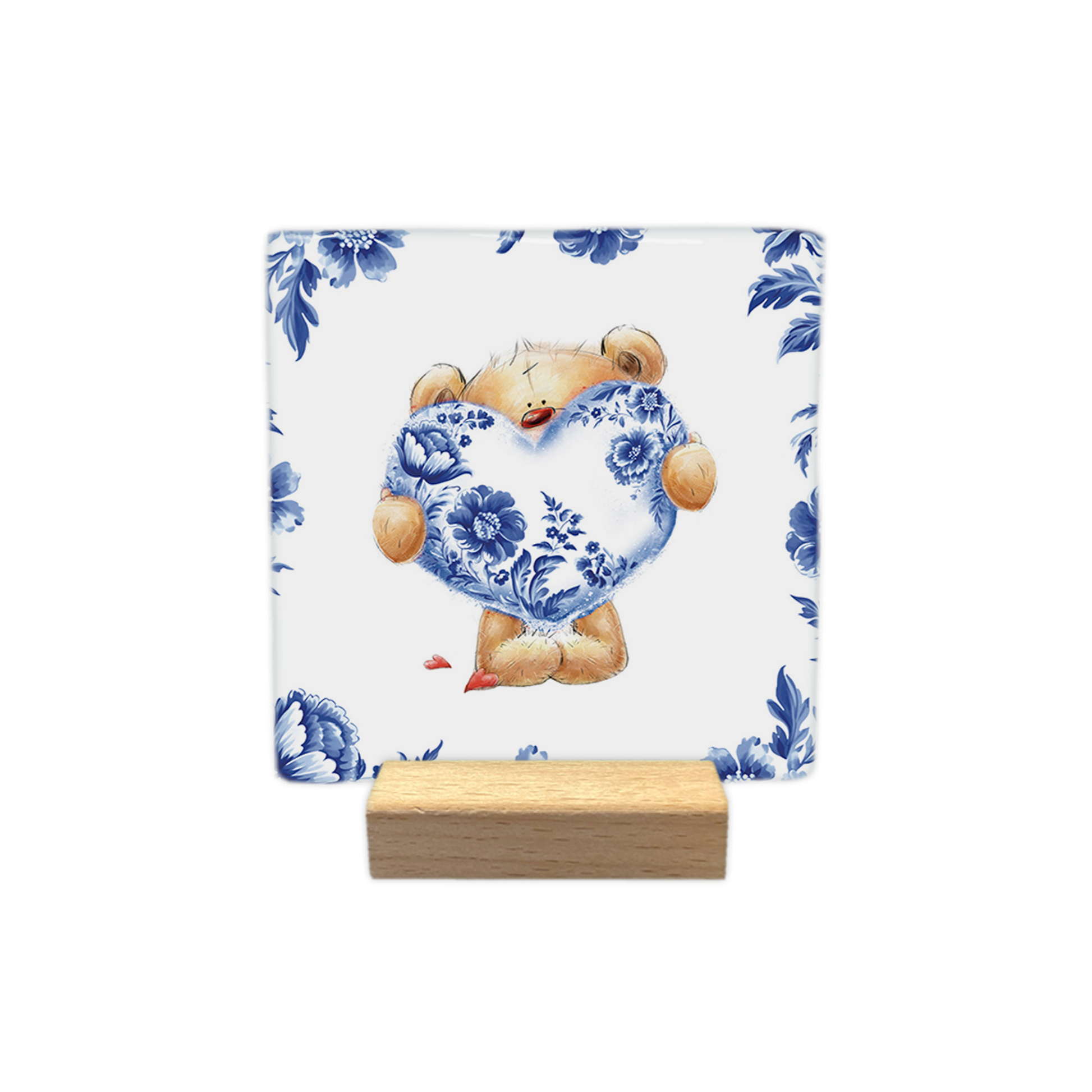 Beertje met Delfts hart - Decoratie tegel - Formaat: - Op deze decoratie tegel staat een knuffelbeer afgebeeld die een groot hart vasthoudt dat gedecoreerd is met een Delfts blauw bloemmotief. De beer is omringd door een rand van dezelfde Delfts blauwe bloemen op een witte achtergrond. Naast de voeten van de beer liggen twee kleine, rode hartjes. - Snelwenskaart
