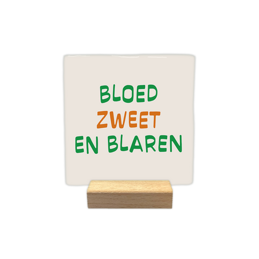 Bloed zweet en bladeren - Decoratie tegel - Formaat: - Op deze decoratie tegel staat de tekst "bloed zweet en blaren" verdeeld over drie regels. De woorden zijn geschreven in een speels lettertype waarbij de eerste en de derde regel in het groen zijn en de middelste regel in het oranje. Het gehele ontwerp is geplaatst op een lichtbeige achtergrond. - Snelwenskaart