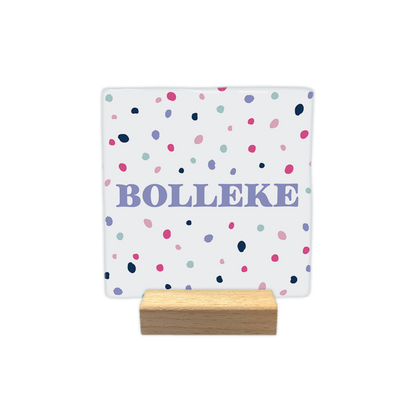 Bolleke - Decoratie tegel - Formaat: - Op deze decoratie tegel staat het woord "bolleke" centraal afgebeeld in lila letters. De achtergrond van de tegel is wit en is versierd met een patroon van kleine, gekleurde stippen in de kleuren roze, donkerblauw, lila en lichtblauw. - Snelwenskaart