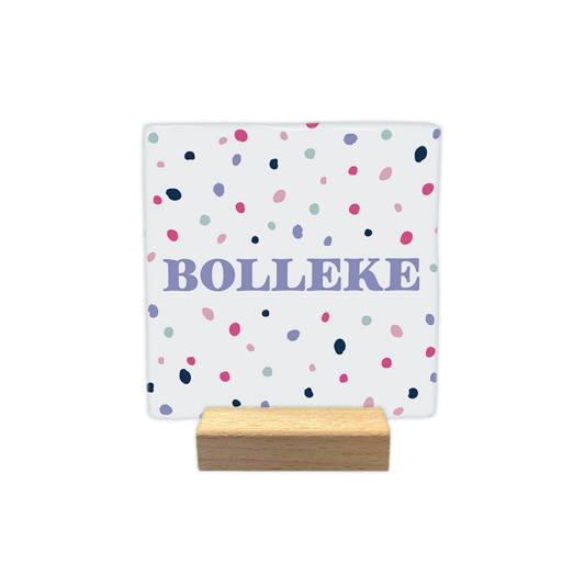Bolleke - Decoratie tegel - Formaat: - Op deze decoratie tegel staat het woord "bolleke" centraal afgebeeld in lila letters. De achtergrond van de tegel is wit en is versierd met een patroon van kleine, gekleurde stippen in de kleuren roze, donkerblauw, lila en lichtblauw. - Snelwenskaart
