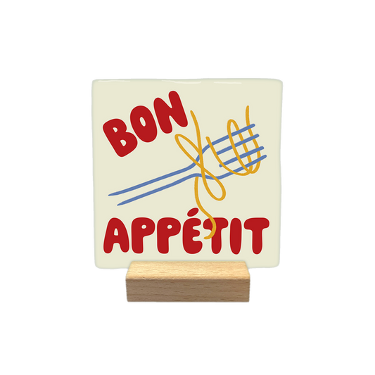Bon appétit - Decoratie tegel - Formaat: - Op deze decoratietegel staat de tekst "BON APPÉTIT" in rode hoofdletters, gescheiden door een illustratie van een vork met daaromheen gewikkelde gele spaghetti. Het ontwerp is geplaatst op een crèmekleurige achtergrond. - Snelwenskaart