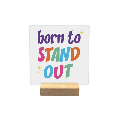Born to stand out - Decoratie tegel - Formaat: - Op deze decoratietegel staat de tekst "born to STAND OUT" in een kleurrijke en speelse typografie. De woorden "STAND" en "OUT" zijn elk opgebouwd uit letters in verschillende kleuren, en het ontwerp is verfraaid met kleine, gele sterretjes. - Snelwenskaart
