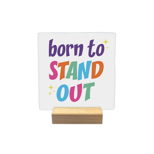 Born to stand out - Decoratie tegel - Formaat: - Op deze decoratietegel staat de tekst "born to STAND OUT" in een kleurrijke en speelse typografie. De woorden "STAND" en "OUT" zijn elk opgebouwd uit letters in verschillende kleuren, en het ontwerp is verfraaid met kleine, gele sterretjes. - Snelwenskaart