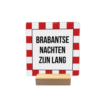 Brabantse nachten zijn lang - Decoratie tegel - Formaat: - Op deze decoratie tegel staat een wit middenvlak met de tekst "Brabantse nachten zijn lang" in donkere letters. Rondom dit centrale vlak bevindt zich een rand met een rood-wit geblokt patroon. Het ontwerp combineert tekst met een opvallende gekleurde omlijsting. - Snelwenskaart