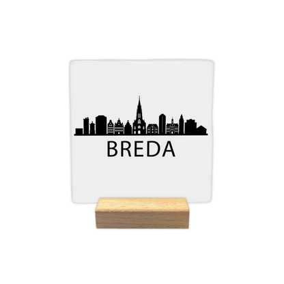 Breda skyline - Decoratie tegel - Formaat: - Op deze decoratie tegel staat een zwarte skyline van Breda afgebeeld tegen een witte achtergrond. Het silhouet bevat diverse herkenbare gebouwen uit de stad. Onder de skyline staat in zwarte letters de naam Breda. Het ontwerp is minimalistisch uitgevoerd in alleen zwart en wit. - Snelwenskaart