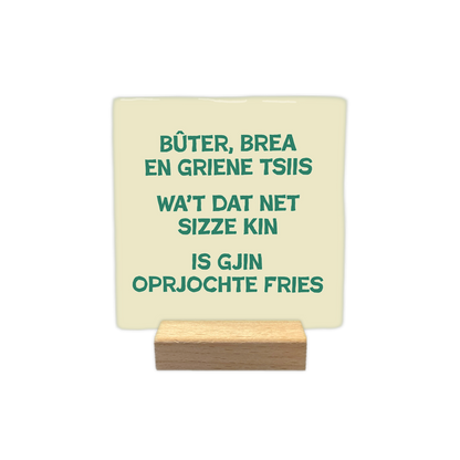 Bûtter, brea en griene tslls - Decoratie tegel - Formaat: - Op deze decoratie tegel staat de tekst "Bûter, brea en griene tsiis, wa't dat net sizze kin is gjin oprjochte Fries" in groene letters centraal afgebeeld. De achtergrond van de tegel is lichtgeel van kleur. - Snelwenskaart