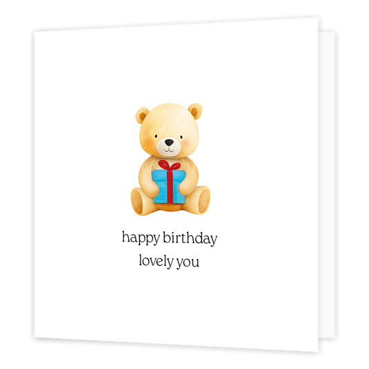 Happy birthday lovely you - Formaat: Klein - Vorm: Vierkant - Verjaardagskaart - Op deze wenskaart staat een getekende teddybeer afgebeeld die recht vooruit kijkt terwijl hij een blauw cadeautje met een rood lint vasthoudt. De beer is lichtbruin van kleur en zit op een witte achtergrond. Onder de illustratie staat de tekst "happy birthday lovely you" in zwarte letters. - Snelwenskaart