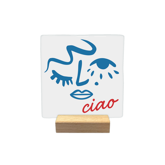 Ciao - Decoratie tegel - Formaat: - Op deze decoratietegel staat een abstracte lijntekening in blauw van een gezicht dat knipoogt. Rechtsonder het gezicht staat het woord "ciao" in rode, cursieve letters. Het ontwerp is gecentreerd op een witte achtergrond. - Snelwenskaart