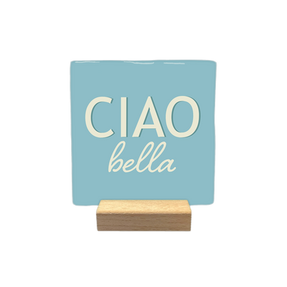 Ciao bella - Decoratie tegel - Formaat: - Op deze decoratietegel staat de tekst "CIAO" in grote, crèmekleurige hoofdletters met daaronder in kleinere, sierlijke letters "bella". Het ontwerp is gecentreerd op een lichtblauwe achtergrond - Snelwenskaart
