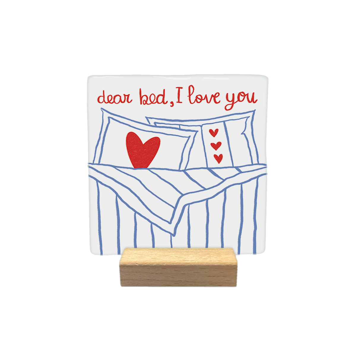 Dear bed, I love you - Decoratie tegel - Formaat: - Op deze decoratietegel staat bovenaan de tekst "dear bed, I love you" in een handgeschreven rood lettertype. Daaronder is een illustratie afgebeeld van een opgemaakt bed met blauw-witte strepen, voorzien van kussens die zijn versierd met rode hartjes. Het ontwerp is gecentreerd op een witte achtergrond. - Snelwenskaart