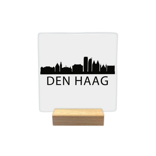 Den Haag skyline - Decoratie tegel - Formaat: - Op deze decoratie tegel staat een zwarte skyline van Den Haag afgebeeld tegen een witte achtergrond. Het silhouet toont diverse herkenbare gebouwen uit de stad. Onder de skyline staat in zwarte letters de plaatsnaam Den Haag. Het gehele ontwerp is uitgevoerd in een minimalistische zwart-witstijl. - Snelwenskaart