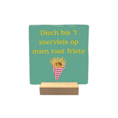 Diech bis 't zoervleis op mien tuut friete - Decoratie tegel - Formaat: - Op deze decoratie tegel staat een lichtgroene achtergrond met daarboven de gele tekst "Diech bis 't zoervleis op mien tuut friete". Onderaan is een afbeelding geplaatst van een rood-wit geblokt frietzakje gevuld met frietjes en een klodder bruine saus. Het ontwerp combineert een tekstuele uiting met een illustratie van een snack. - Snelwenskaart