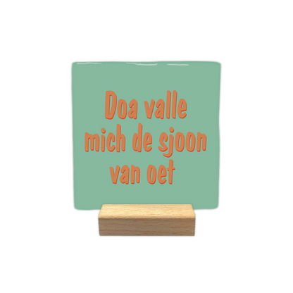 Doa valle mich de sjoon van oet - Decoratie tegel - Formaat: - Op deze decoratie tegel staat de tekst "Doa valle mich de sjoon van oet" in oranje letters met een subtiele schaduwrand. De tekst is verdeeld over drie regels en geplaatst op een mintgroene achtergrond. Het lettertype oogt vriendelijk en speels. - Snelwenskaart